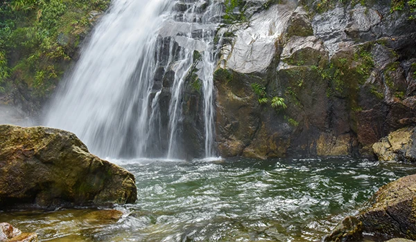 Cachoeira em meio à natureza com águas cristalinas e rochas ao redor, um cenário tranquilo e perfeito para atividades ao ar livre.