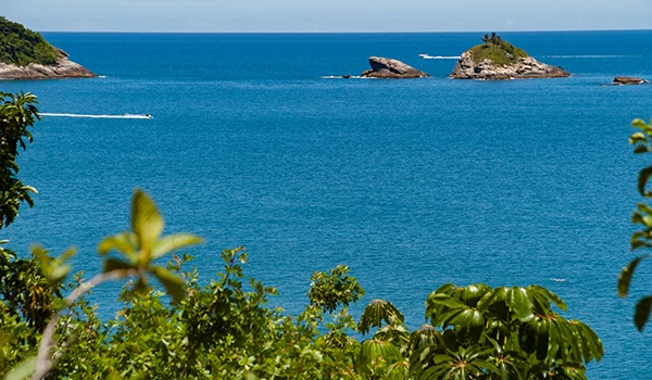 Praia com águas azul-turquesa, pequenas ilhas ao fundo e vegetação exuberante na orla, ideal para turismo e lazer no litoral brasileiro.