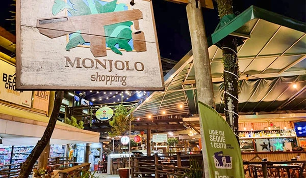 Fachada do restaurante Monjolo Shopping com decoração ao ar livre e sinalização que incentiva a economia de seque e custo, ambiente animado à noite