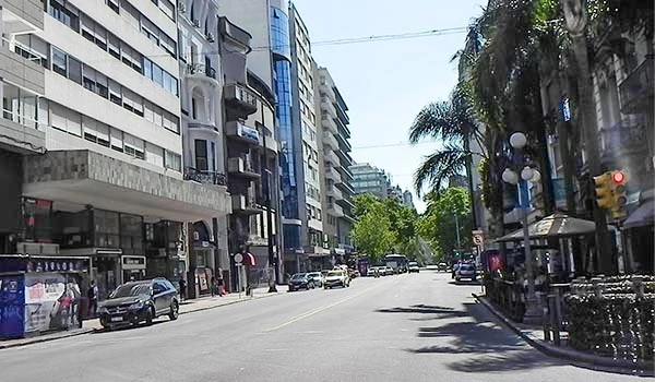 Imagem de uma rua no centro de uma cidade moderna, com prédios altos, árvores e movimento de veículos e pedestres. Perfeito para quem busca dicas de locais para visitar na cidade. O que fazer em Montevidéu.