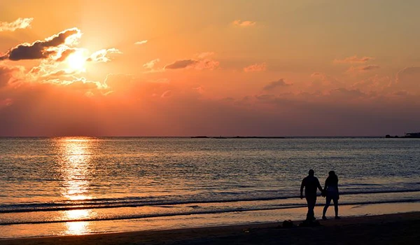 Casal caminhando na praia ao pôr do sol, criando uma cena romântica e serena.