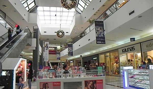 Interior de shopping center moderno com lojas de luxo, escadas rolantes, área de decoração natalina e visitantes passeando nas dependências.