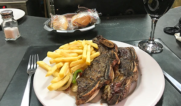 Filé de carne com batatas fritas em um prato de jantar, acompanhado de vinho tinto e pão, ideal para uma refeição deliciosa e sofisticada.