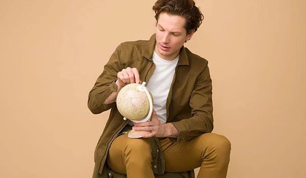 Homem segurando um globo terrestre, contemplando suas dimensões e detalhes com expressão pensativa. Dicas para presente quem gosta de viajar.