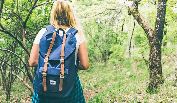 Uma mulher de costas caminhando em uma trilha na floresta, usando uma mochila azul. Dicas para presente quem gosta de viajar.