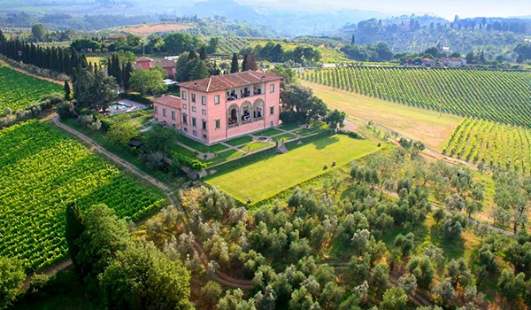 Vista aérea de uma elegante villa italiana cercada por jardins, oliveiras e extensos vinhedos nas colinas. Lua de Mel na Itália.