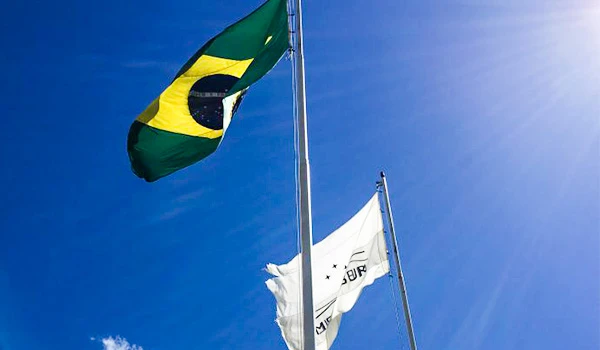 Bandeira do Brasil e uma bandeira branca tremulam ao vento sob um céu azul claro, representando o patriotismo e a identidade brasileira em um dia ensolarado. Lua de Mel em Brasília.