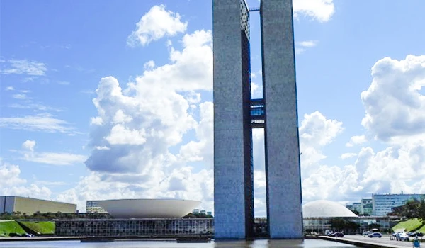 Imagem do Congresso Nacional do Brasil em Brasília, com seus prédios altos e céu com nuvens. Destaca a arquitetura moderna do edifício em forma de dois pilares paralelos.