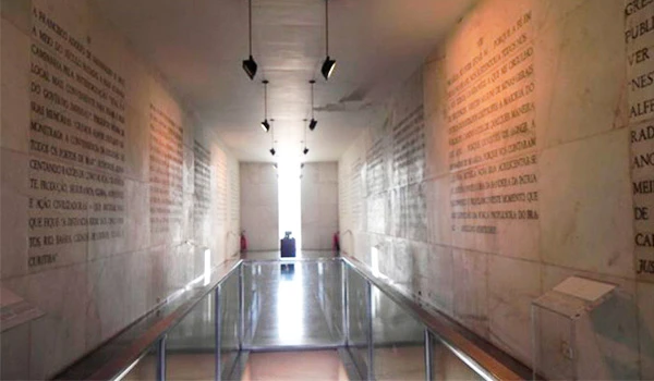 Imagem de um corredor do Museu de Brasília com paredes de pedra contendo textos históricos, iluminação suave e um ambiente de reflexão.