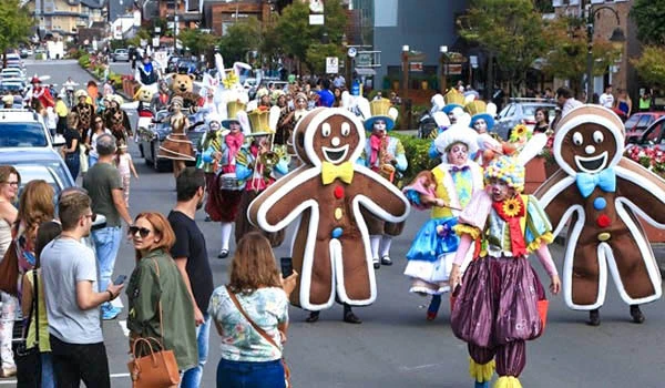 Desfile de carnaval com pessoas fantasiadas de personagens coloridos, incluindo gingerbreads gigantes e adereços alegres, em uma rua movimentada.