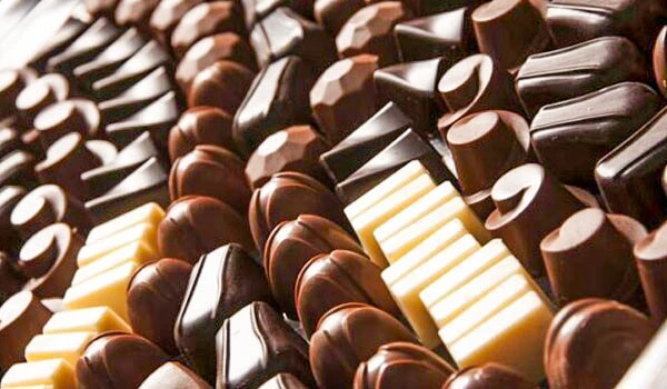 Variedade de chocolates de differentes tipos e cores, incluindo escuros, ao leite e brancos, dispostos em fila organizada.