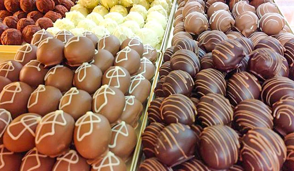 Trio de diferentes tipos de trufas de chocolate expostas em loja, com diversas decorações e sabores variados, atrativas e deliciosas.