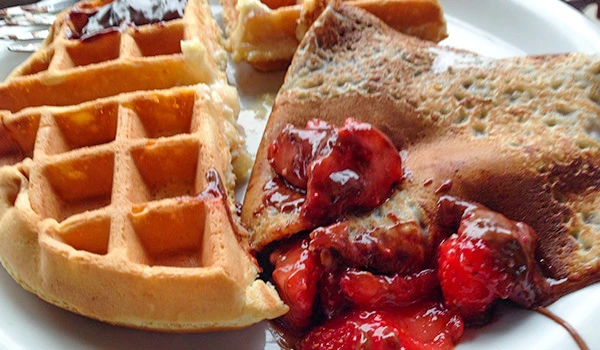 Imagem de waffles dourados com frutas vermelhas e um crepe recheado com geleia de frutas vermelhas, perfeito para café da manhã ou brunch.