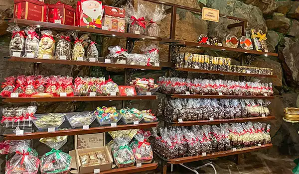 Vitrine com produtos de Natal, incluindo bolas, biscoitos decorados e lembrancinhas, tudo organizado em prateleiras de madeira para festas de fim de ano.