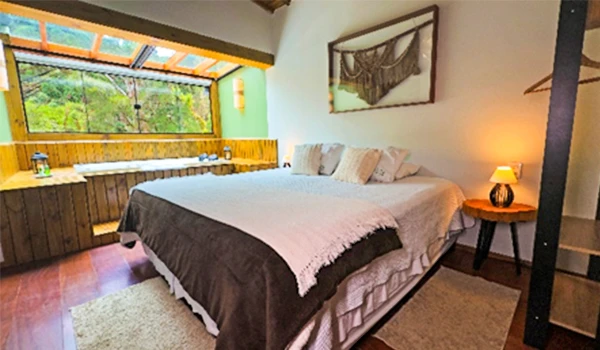 Quarto de casal aconchegante com iluminação natural, decoração moderna e vista para a natureza, ideal para relaxar e descansar.