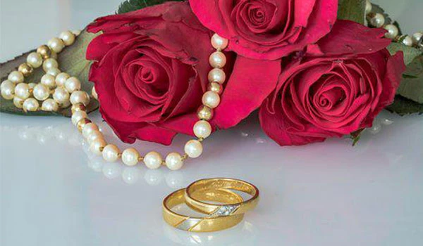 Imagem de alianças de casamento com rosas vermelhas e pérolas, simbolizando amor e união. Ideal para celebrações de casamentos e noivados.
