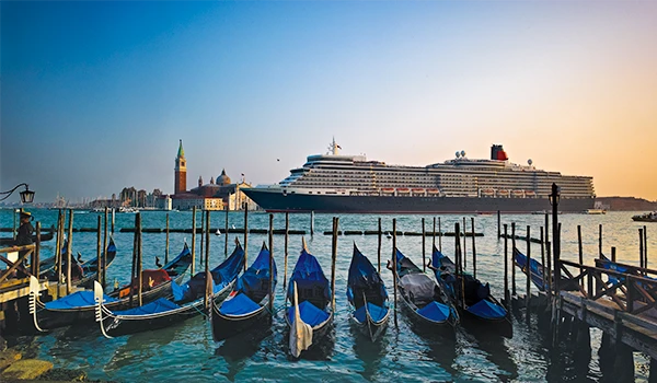 Vista deslumbrante de um cruzeiro gigantesco ancorado em Veneza, com gôndolas tradicionais em primeiro plano, refletindo a beleza da cidade.