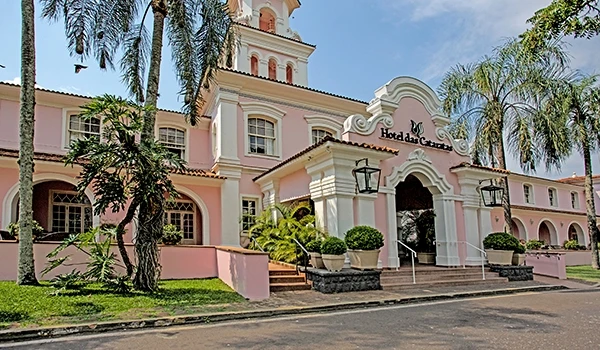 Fachada do Hotel das Cataratas, em estilo colonial, com suas paredes cor de rosa, rodeado por palmeiras e jardins bem cuidados. Lugares para comemorar aniversário de casamento.