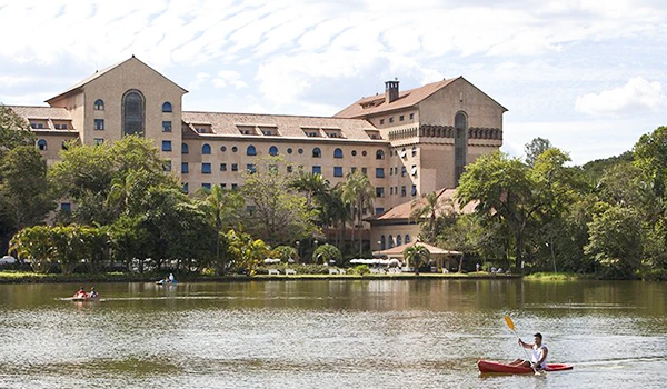 Foto do Grande Hotel de Araxá com a construção, tendo um bonito lago a frente com um homem praticando canoagem.