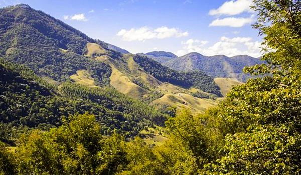 Paisagem montanhosa com colinas verdes sob um céu claro, ideal para quem ama a natureza, ideal para a Lua de mel em Minas Gerais.