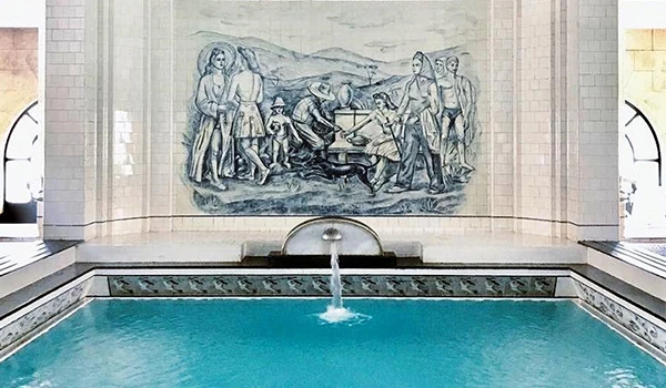 Foto do SPA de Araxá, com pintura mural retratando atividades rurais e uma fonte em um ambiente de piscina com água azul, enfatizando a cultura e a arte.