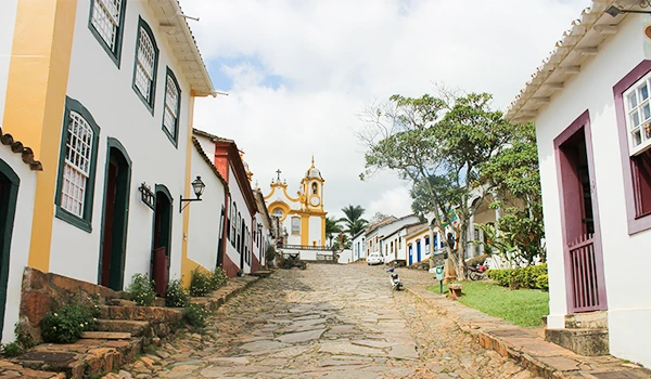 Uma típica rua de Tiradentes com suas casas coloniais coloridas e a igreja ao fundo, mostrando a arquitetura histórica e o charme da cidade.