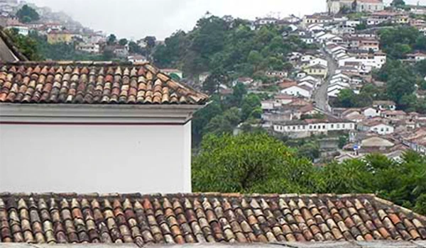Vista panorâmica com telhados em uma paisagem montanhosa e urbana, destacando a harmonia entre a arquitetura e a natureza em Ouro Preto.