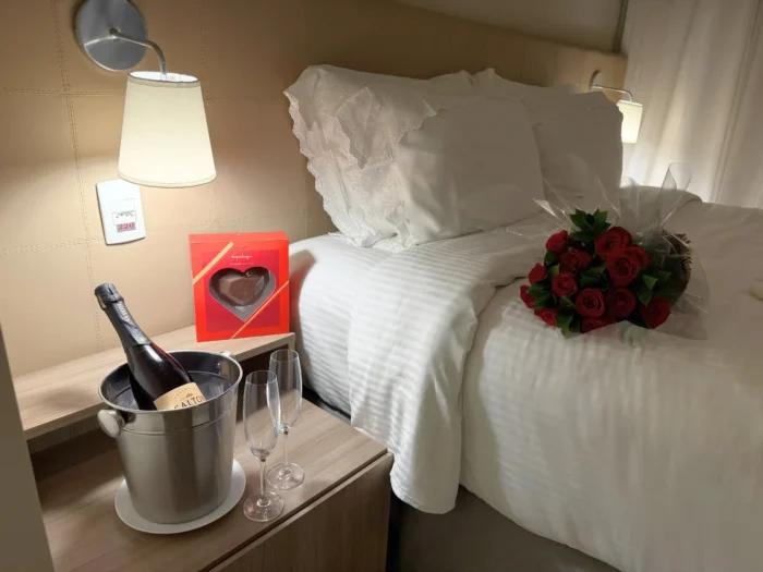 Staybridge Suites – Cidade de São Paulo, cama com buquê de rosas vermelha, ao lado espumante e chocolate para o Dia dos Namorados.
