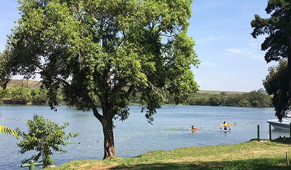 Paisagem de um rio tranquilo com árvores verdes e barcos ao longe, cenário perfeito para lazer ao ar livre em um dia ensolarado no Brasil. Viagem à Botucatu e Barra Bonita.