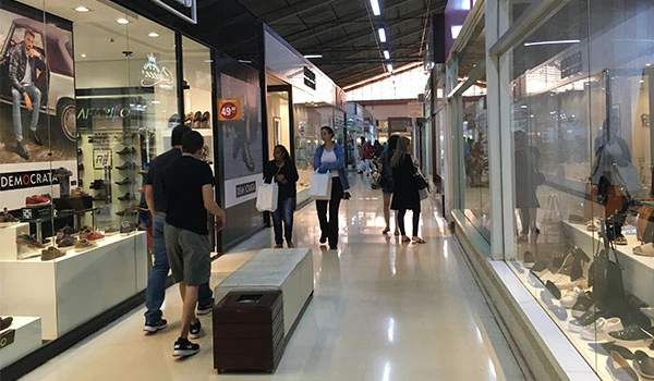 Visão de shopping center com lojas de roupas e acessórios, pessoas caminhando e fazendo compras em ambiente moderno.