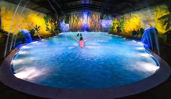 Visão deslumbrante de uma piscina iluminada com águas azuladas e cascatas, criando um ambiente tropical relaxante. Ideal para momentos de lazer e descanso em Brotas, uma das cidades do interior de SP.