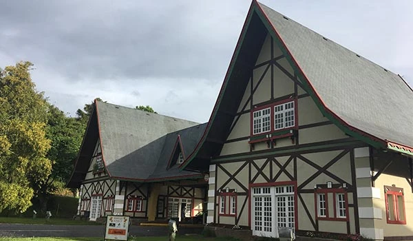 Imagens de uma arquitetura de estilo enxaimel, destacando casas com telhados inclinados e janelas grandes. Esta construção é típica das influências alemãs no Brasil, refletindo a cultura e tradições da região.