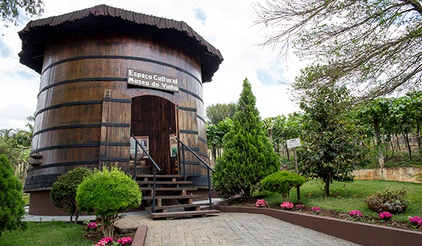 Exterior do Espaço Cultural Museu do Vinho, com um barril de madeira e área ajardinada. Um dos lugares baratos para Lua de Mel em SP.