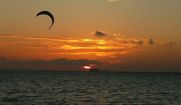 Imagem de um pôr do sol com céu alaranjado e uma lua crescente em horizonte sobre o mar, perfeita para apreciar a tranquilidade do entardecer.
