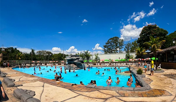 Atraente piscina com muitas pessoas se divertindo, rodeada por natureza e espreguiçadeiras em um dia ensolarado. Ideal para momentos de lazer e relaxamento.