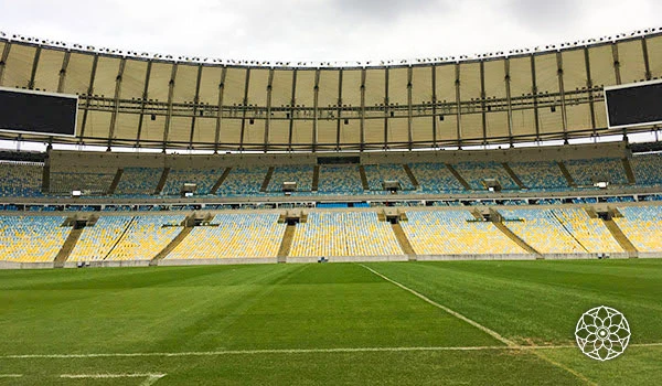 Estádio de futebol vazio com arquibancadas coloridas, campo bem cuidado e céu nublado, ideal para partidas de futebol e eventos esportivos ao ar livre.