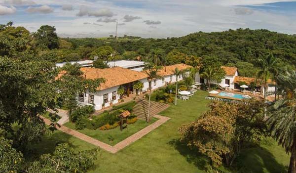Foto aérea da Fazenda Capoava  no interior de SP, uma construção em formato de casa grande histórica cercada de muita vegetação.