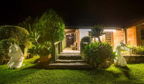Foto noturna do hotel com fachada estilo casa, com 2 estátuas de cavalos brancos na área do jardim, no interior de SP.