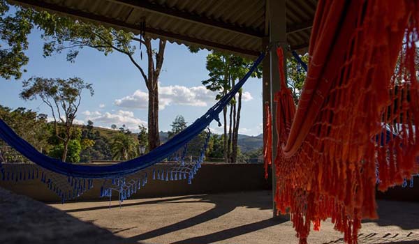 Foto de 2 redes coloridas em uma varanda, cercada de vegetação, de um hotel fazenda com passeio a cavalo 
