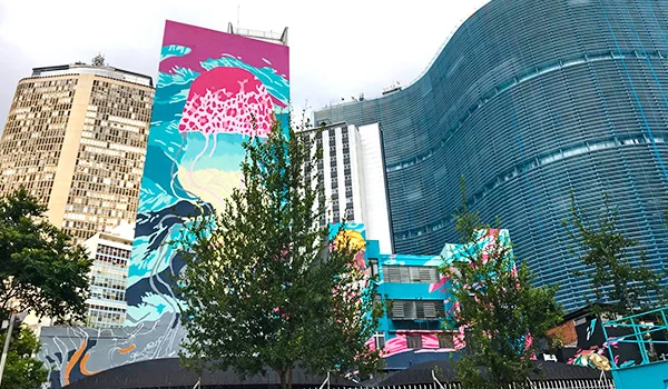 Edifícios urbanos em São Paulo, incluindo uma fachada curva azul de vidro e um prédio decorado com grandes murais coloridos de arte urbana, com destaque para uma ilustração de águas-vivas.