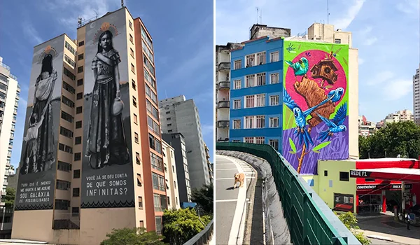 Fotografia de dois edifícios urbanos em São Paulo decorados com grandes murais de arte urbana. À esquerda, fachadas exibem figuras femininas em preto e branco acompanhadas de frases em português. À direita, um prédio azul apresenta um mural colorido com aves tropicais, flores e elementos da natureza. Em primeiro plano, uma via elevada com grades verdes, sob um céu azul parcialmente nublado.