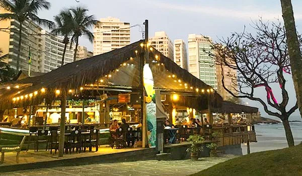 Praia com reconstrução de bar e restaurante em estilo tropical, iluminação aconchegante e palmeiras ao fundo, ideal para quem busca uma experiência gastronômica à beira-mar.