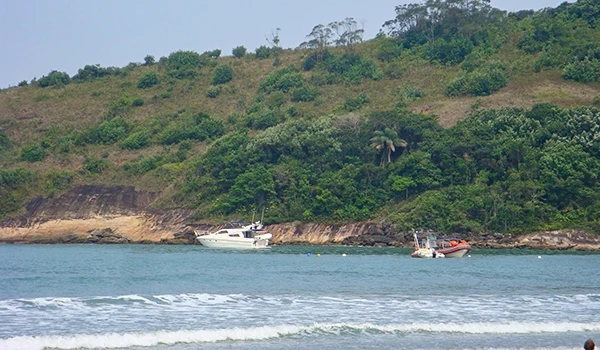 Praia tranquila com barcos ancorados em águas calmas e vegetação ao fundo, proporcionando um cenário relaxante e natural.