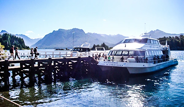 Passeio de barco em um lago com montanhas ao fundo e pessoas aproveitando a vista em um dia ensolarado na natureza