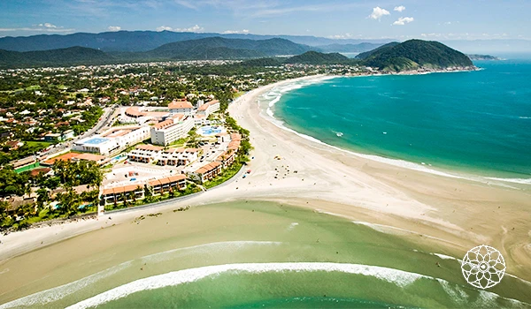 Vista aérea deslumbrante de uma praia tranquila, com águas cristalinas, areia clara e um resort luxuoso ao fundo, perfeita para lua de mel.