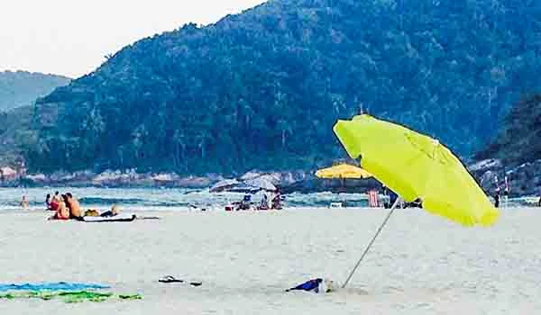Praia tranquila com guarda-sol amarelo e montanhas ao fundo, ideal para relaxar e aproveitar o sol. Perfeito para quem busca descanso à beira-mar.