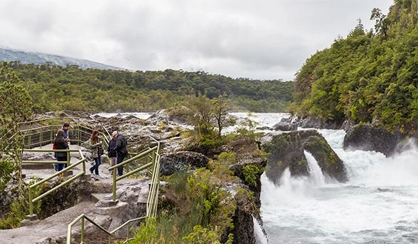 Cachoeira e trilha de turismo ecológico em meio à natureza exuberante, com visitantes explorando a paisagem natural e curtindo a vista. Travessia dos Lagos Andinos.