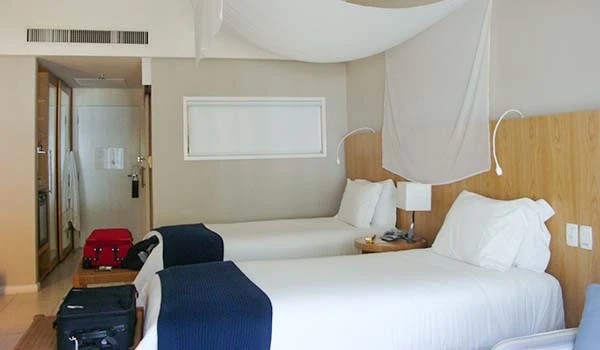Quarto de hotel com duas camas, decoração contemporânea e iluminação suave. Dicas da Lua de Mel no Jequitimar Guarujá.