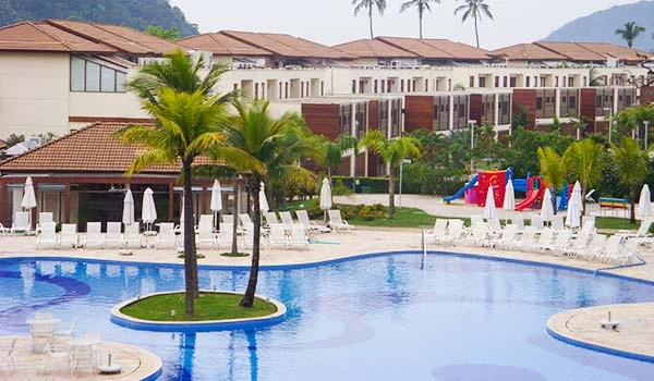 Vista de um resort tranquilo com piscina, palmeiras e acomodação confortável. Dicas da Lua de Mel no Jequitimar Guarujá.