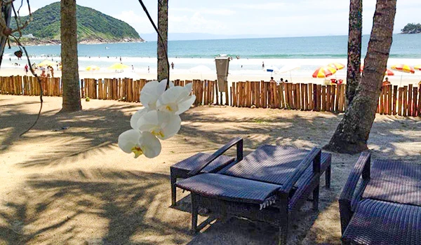 Uma bela praia com cadeiras de sol, árvores e um fundo sereno. É um lugar perfeito para relaxar e desfrutar do mar. Dicas da Lua de Mel no Jequitimar